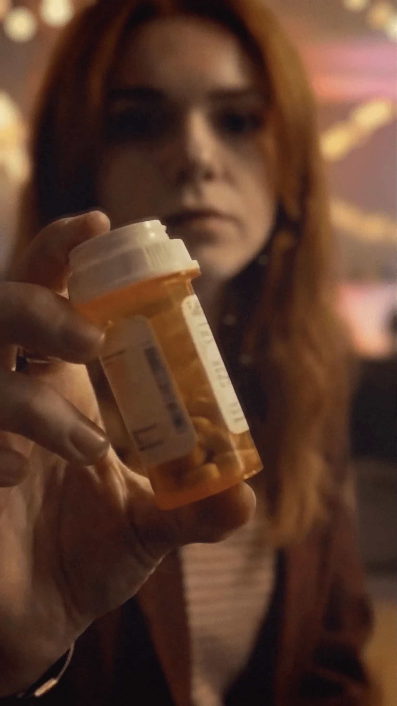 A young woman holds a prescription pill bottle at a party
